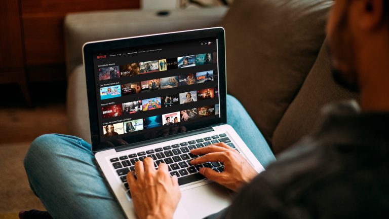 Eine Person sitzt vor einem Laptop. Auf dem Bildschirm ist das Hauptmenü von Netflix zu sehen.