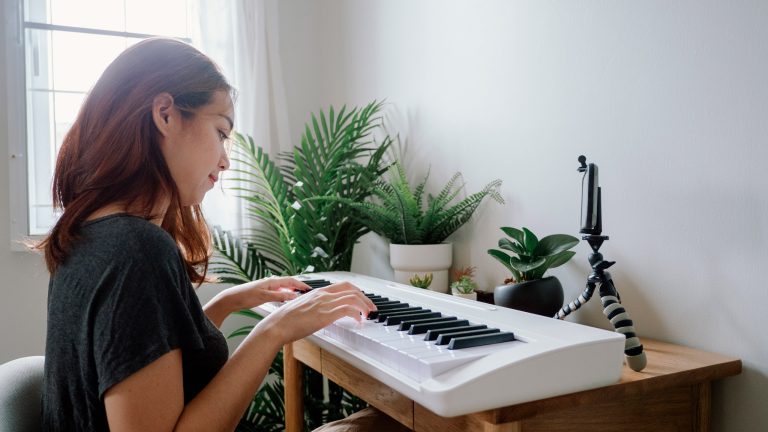 Eine Person sitzt vor einem Keyboard, auf dem Tisch ist au&szlig;erdem ein Smartphone in einer Halterung zu sehen.