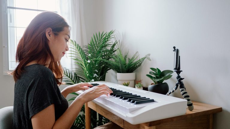 Eine Person sitzt vor einem Keyboard, auf dem Tisch ist außerdem ein Smartphone in einer Halterung zu sehen.