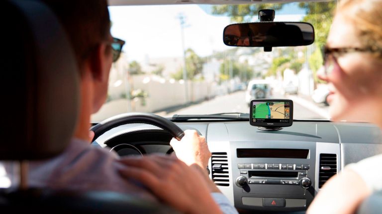 Zwei Personen sitzen in einem Auto. Auf dem Dashboard ist ein Navigationssystem zu sehen.