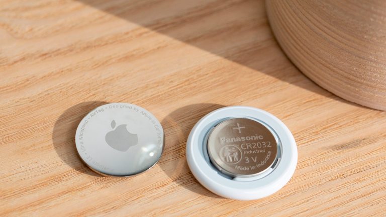 Ein geöffneter Apple AirTag, in dem die Knopfzelle zu sehen ist. Der silberne Deckel liegt daneben.