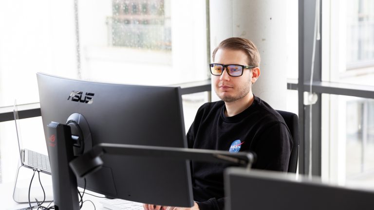 Eine Person sitzt an einem Rechner und trägt eine Computerarbeitsbrille.
