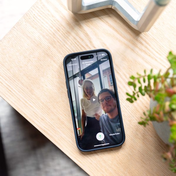 Ein iPhone 14 Pro liegt auf einem Holztisch. Auf dem Bildschirm ist eine Videonachricht bei FaceTime zu sehen.