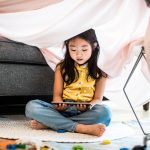 Ein Kind sitzt unter einer Decke, die &uuml;ber ein Sofa gespannt ist und schaut sich etwas auf einem Tablet an.