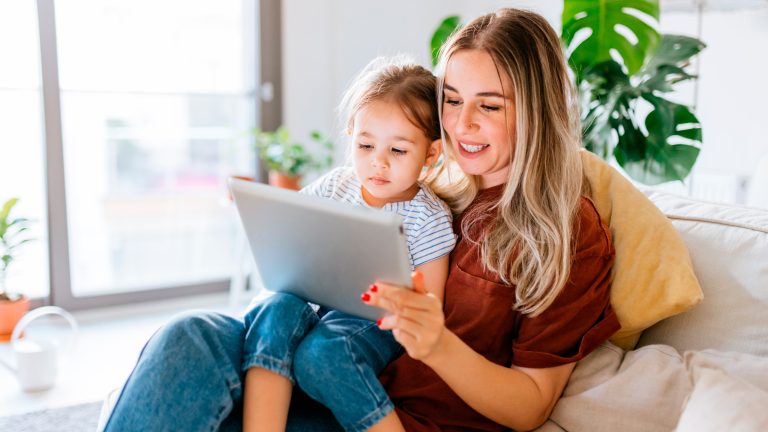 Eine Person und ein Kind sitzen zusammen auf einem Sofa und bedienen ein Tablet.