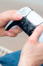 Eine Person hält einen weißen Dualsense-Controller der PS5 in der Hand.