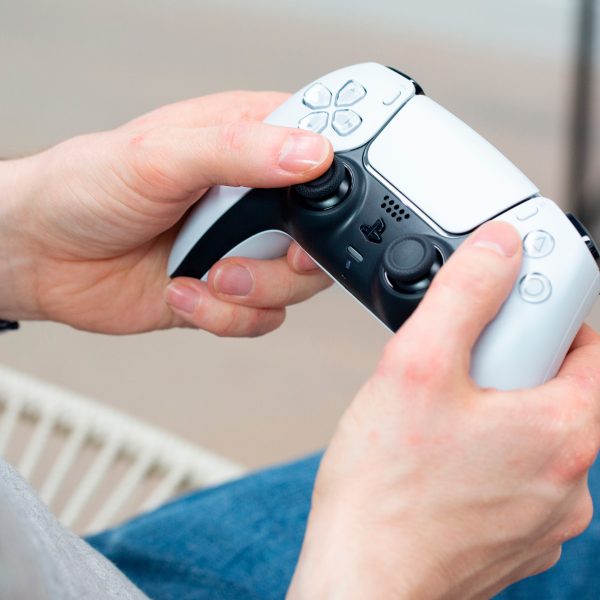Eine Person h&auml;lt einen wei&szlig;en Dualsense-Controller der PS5 in der Hand.