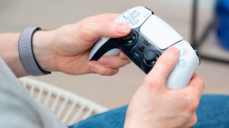 Eine Person hält einen weißen Dualsense-Controller der PS5 in der Hand.