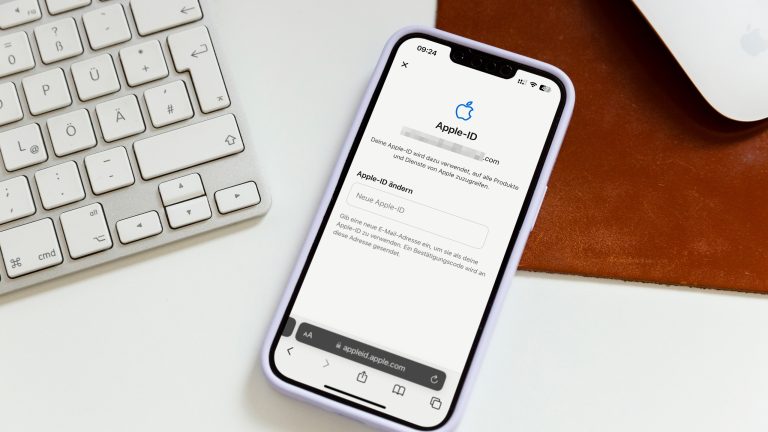 Ein iPhone mit geöffneter Apple-ID-Seite liegt neben einer Tastatur auf einem Schreibtisch.