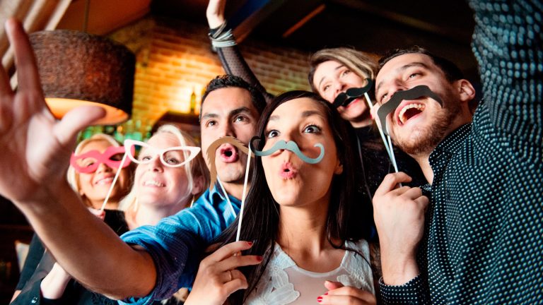 Eine Gruppe von Personen hält sich Party-Requisiten vors Gesicht und schneidet Grimassen in die Kamera.