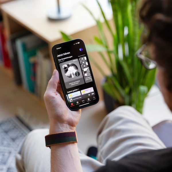 Eine Person h&auml;lt ein iPhone in der Hand, auf dem die Musik-App im Dunkelmodus angezeigt wird.