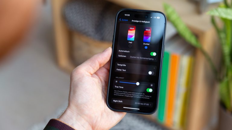 Eine Person h&auml;lt ein iPhone in der Hand, auf dem die Einstellungen f&uuml;r den Dunkelmodus ge&ouml;ffnet sind.