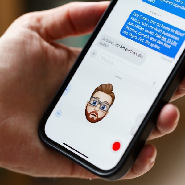 Eine Person h&auml;lt ein iPhone in der Hand, auf der ein Memoji den Gesichtsausdruck der Person nachahmt.