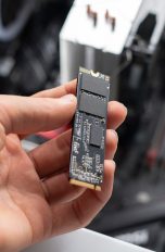 Eine Person hält eine M.2-SSD über einen geöffneten Desktop-PC.