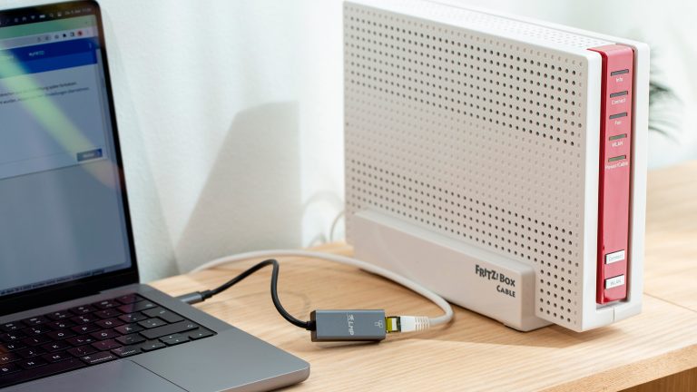 Eine FRITZ!Box 6690 Cable steht auf einem Regal. Per LAN-Kabel ist ein MacBook Pro angeschlossen.