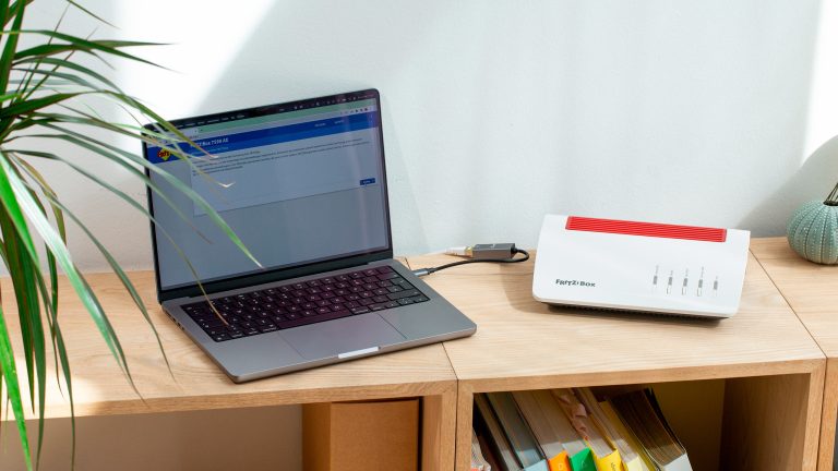 Eine FRITZ!Box 7590 AX steht auf einem Regal. Angeschlossen an den Router ist ein MacBook Pro.