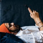 Eine Person liegt auf einem Sofa und schaut in ihr Smartphone.