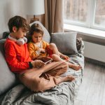 Zwei Kinder sitzen auf einem Sofa und schauen zusammen etwas auf einem Smartphone.