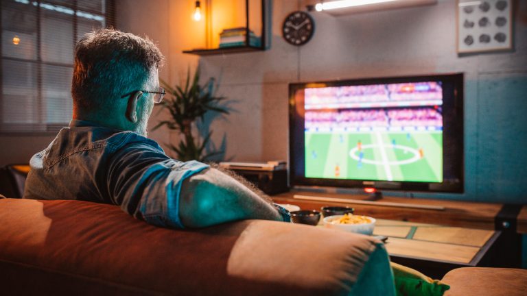 Eine Person sitzt auf dem Sofa und schaut ein Fußball-Spiel.