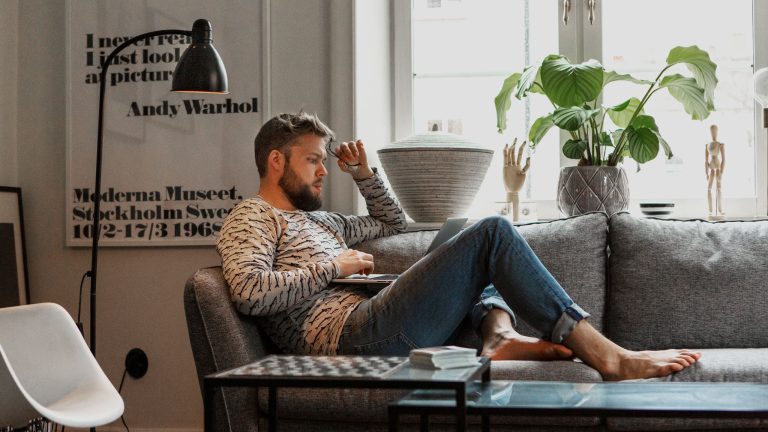 Eine Person sitzt auf einem Sofa und bedient einen Laptop.