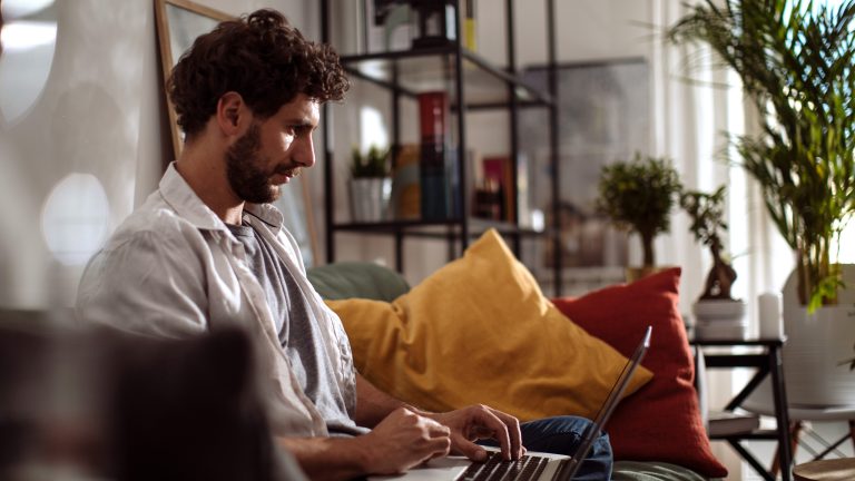 Eine Person sitzt auf einem Sofa und bedient einen Laptop.