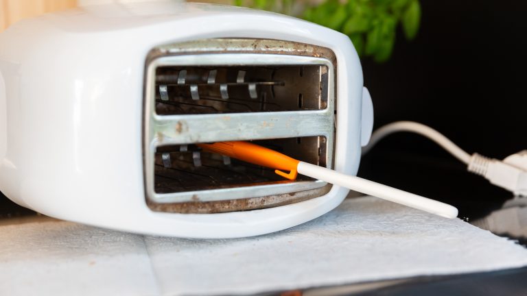 Ein weißer Toaster liegt auf der Seite. Ein Backpinsel steckt teilweise im Innern des Geräts.