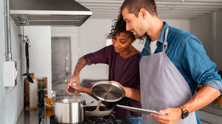 Zwei Personen stehen zusammen an einem Herd und kochen etwas.