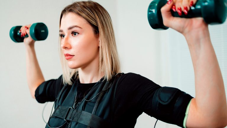 Nahaufnahme einer Person, die mit Kurzhanteln ein EMS-Training absolviert. Nahaufnahme einer Person, die mit Kurzhanteln ein EMS-Training absolviert.