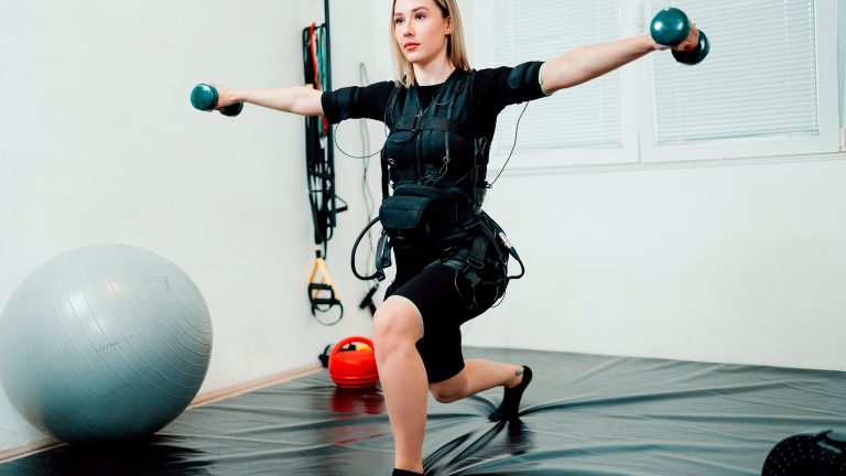 Eine Person macht eine Übung mit Kurzhanteln und trägt dabei ein EMS-Gerät. Eine Person macht eine Übung mit Kurzhanteln und trägt dabei ein EMS-Gerät.