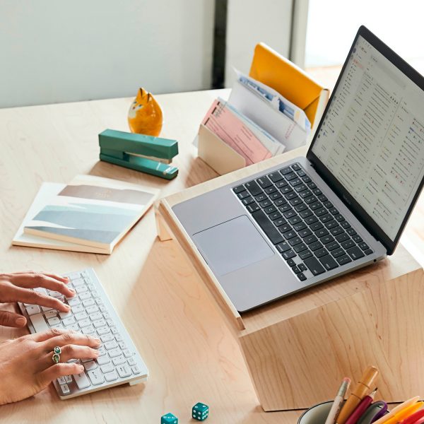 Ein MacBook Pro steht auf einem Laptop-Ständer auf einem Schreibtisch. Davor tippt eine Person auf einem Magic Keyboard.
