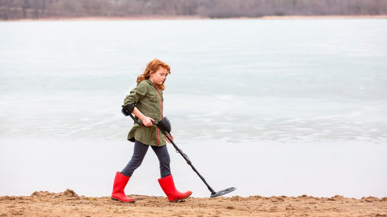 Ein Kind läuft mit einem Metalldetektor einen Strand entlang.