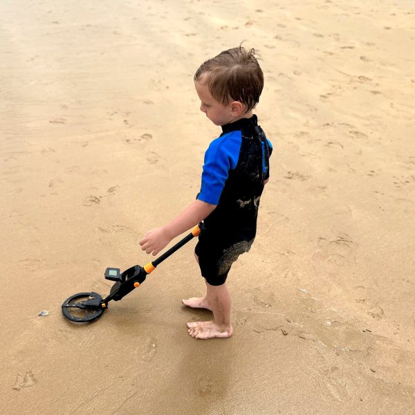 Ein Kind sondelt mit einem Metalldetektor am Strand.