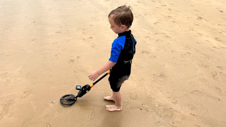Ein Kind sondelt mit einem Metalldetektor am Strand.