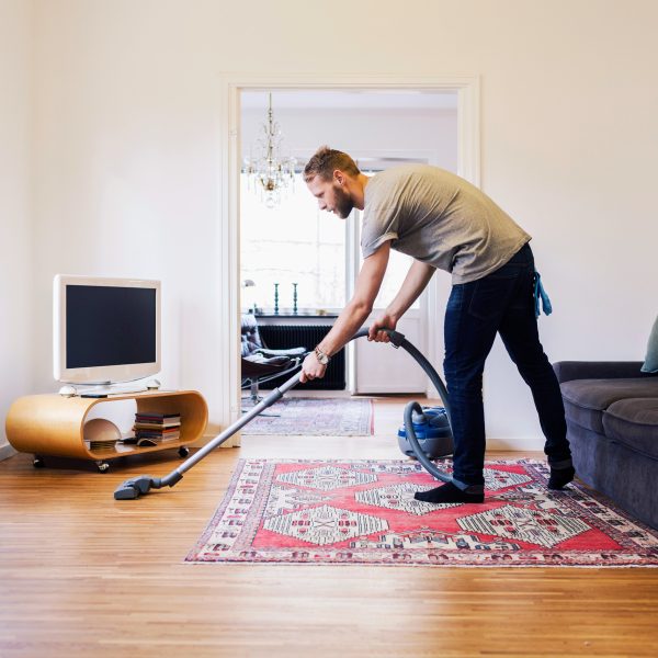 Eine Person saugt mit einem Staubsauger ein Wohnzimmer.