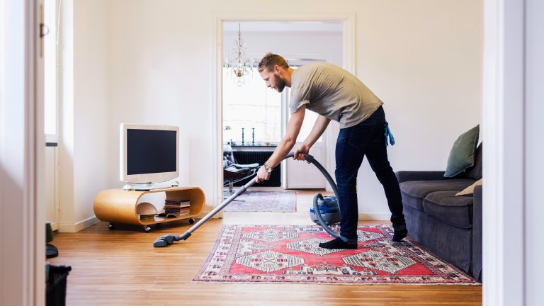 Eine Person saugt mit einem Staubsauger ein Wohnzimmer.