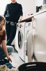 Eine Person kniet vor einem Wäschetrockner und hebt Wäsche auf.
