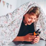 Ein Kind unter einer Bettdecke h&auml;lt ein Walkie-Talkie in der Hand.