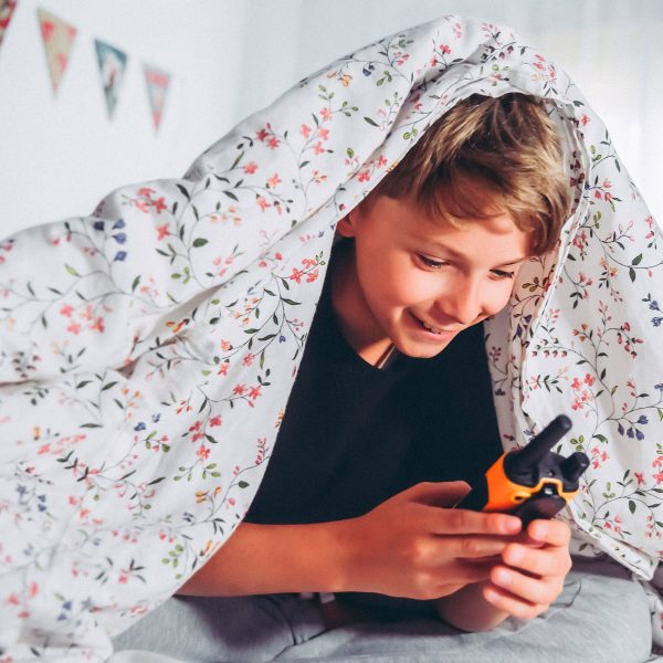 Ein Kind unter einer Bettdecke h&auml;lt ein Walkie-Talkie in der Hand.