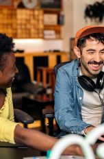 Zwei Personen sitzen in einem Studio vor einem Rechner. Eine von ihnen hat Kopfh&ouml;rer um den Hals h&auml;ngen.