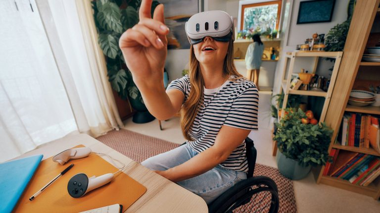 Eine Person sitzt an einem Tisch, auf dem ein Controller der Meta Quest 3 liegt. Die VR-Brille, die die Person trägt, bedient sie mit einer nach oben zeigenden Hand.