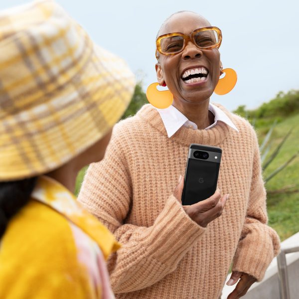 Eine Person h&auml;lt ein Google Pixel 8 in der Hand und lacht. Neben ihr steht ein Kind.