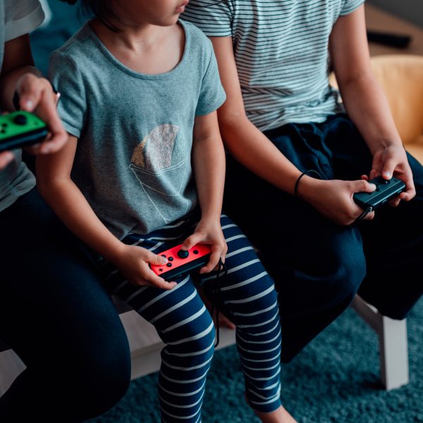 Drei j&uuml;ngere Personen sitzen auf einem Tisch. In den H&auml;nden halten sie jeweils einen Nintendo Joy-Con.