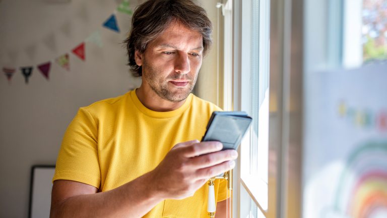 Eine Person lehnt in einem Kinderzimmer an einem Fenster und schaut auf ein Smartphone.
