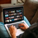 Eine Person sitzt an einem MacBook. Auf dem Display ist die Website von Netflix zu sehen.