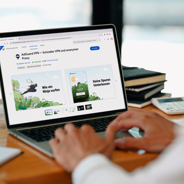Person vor Laptop auf einem Office-Schreibtisch. Der ge&ouml;ffnete Google Chrome Browser zeigt die Erweiterung &bdquo;AdGuard VPN&ldquo; im &bdquo;Chrome Web Store&ldquo;.