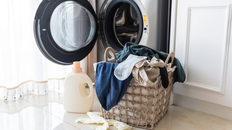Ein Korb voller Wäsche steht vor einer geöffneten Waschmaschine.