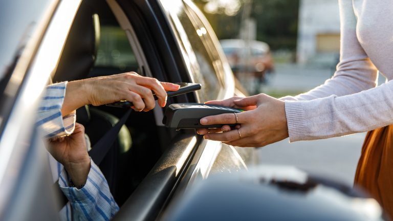 Eine Person hält ihr Smartphone aus dem Fenster eines Autos auf ein Kartenlesegerät.