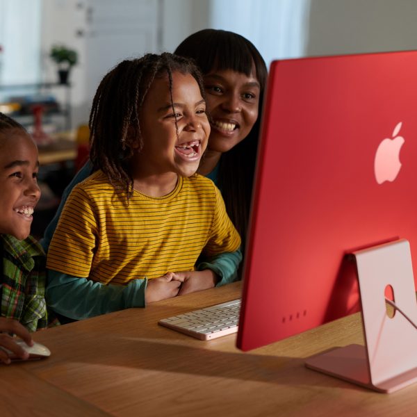 Zwei Kinder und eine erwachsene Person sitzen vor einem iMac.