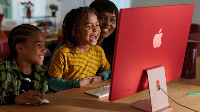 Zwei Kinder und eine erwachsene Person sitzen vor einem iMac.