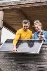 Zwei Personen bringen auf einem Balkon eine kompakte Photovoltaikanlage an. Zwei Personen bringen auf einem Balkon eine kompakte Photovoltaikanlage an.